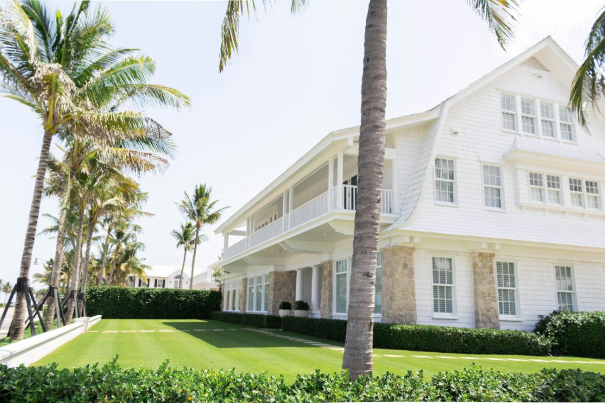 A white wooden home framed by palm trees in coastal Florida